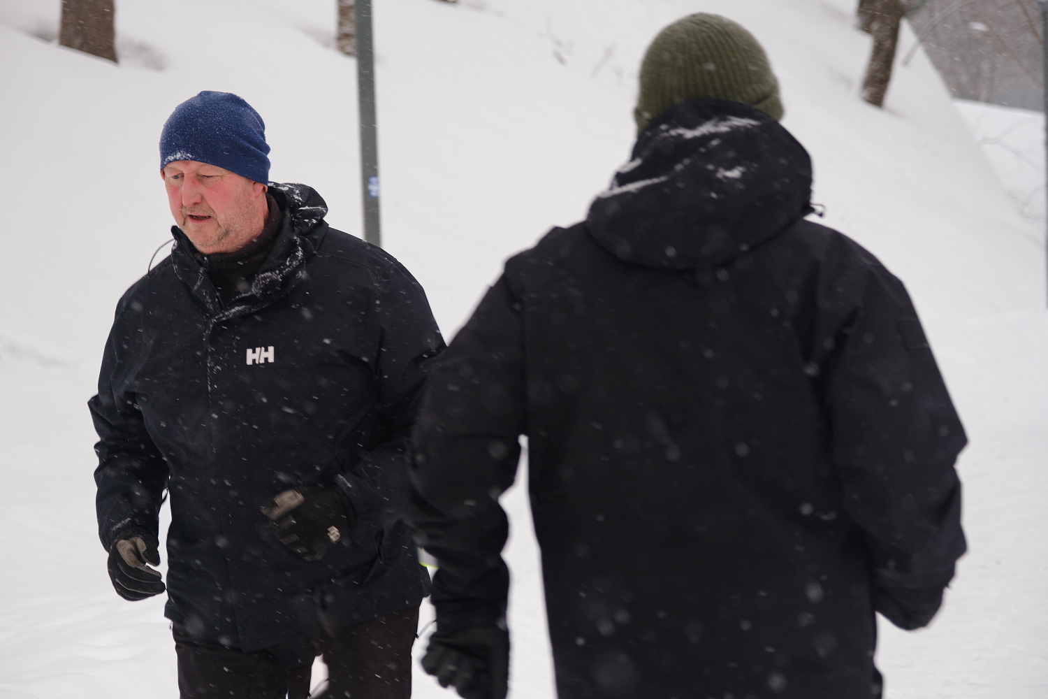 En mann i svarte klær og lue løper ute i snøen. En annen mann løper motsatt vei. 