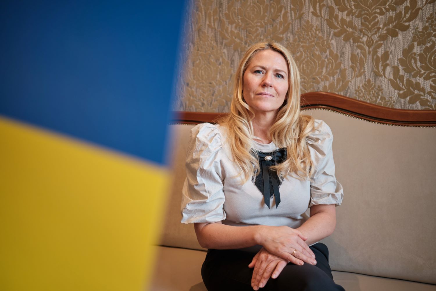 Monica Myrvold Berg sitter i sofaen på hennes kontor, med ukrainsk flagg i bakgrunnen