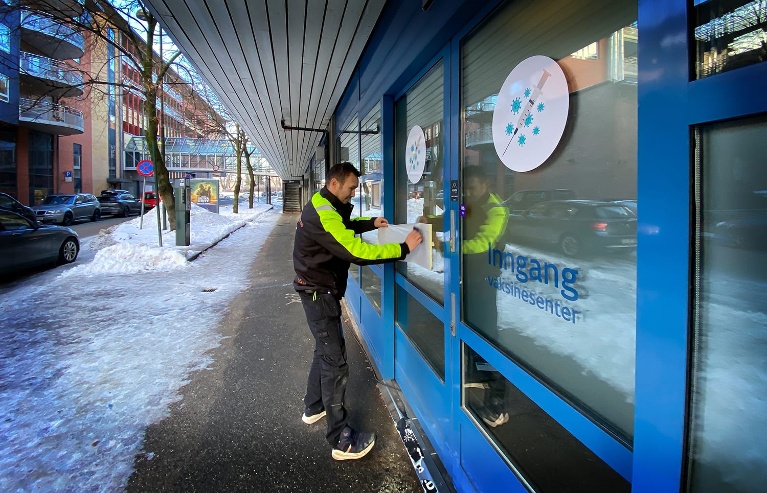 Mann monterer folie med Drammen kommunes logo på døra inn til vaksinesenteret i Thamsgate 5.