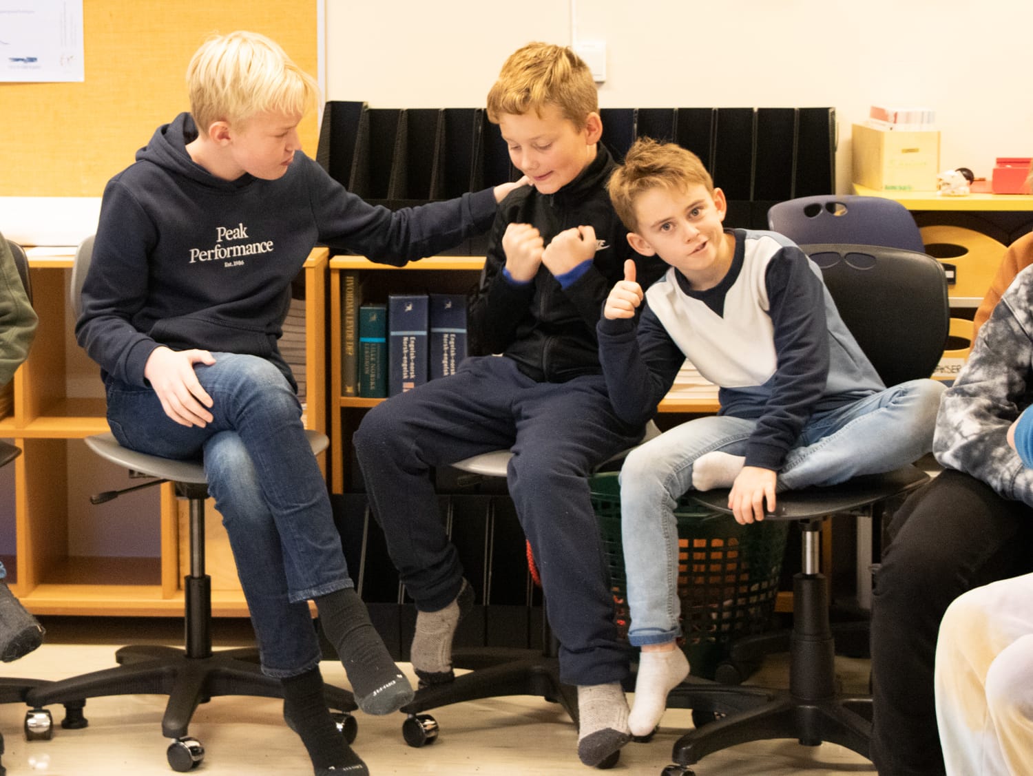 Tre gutter sitter på stoler i et klasserom og er veldig fornøyd.