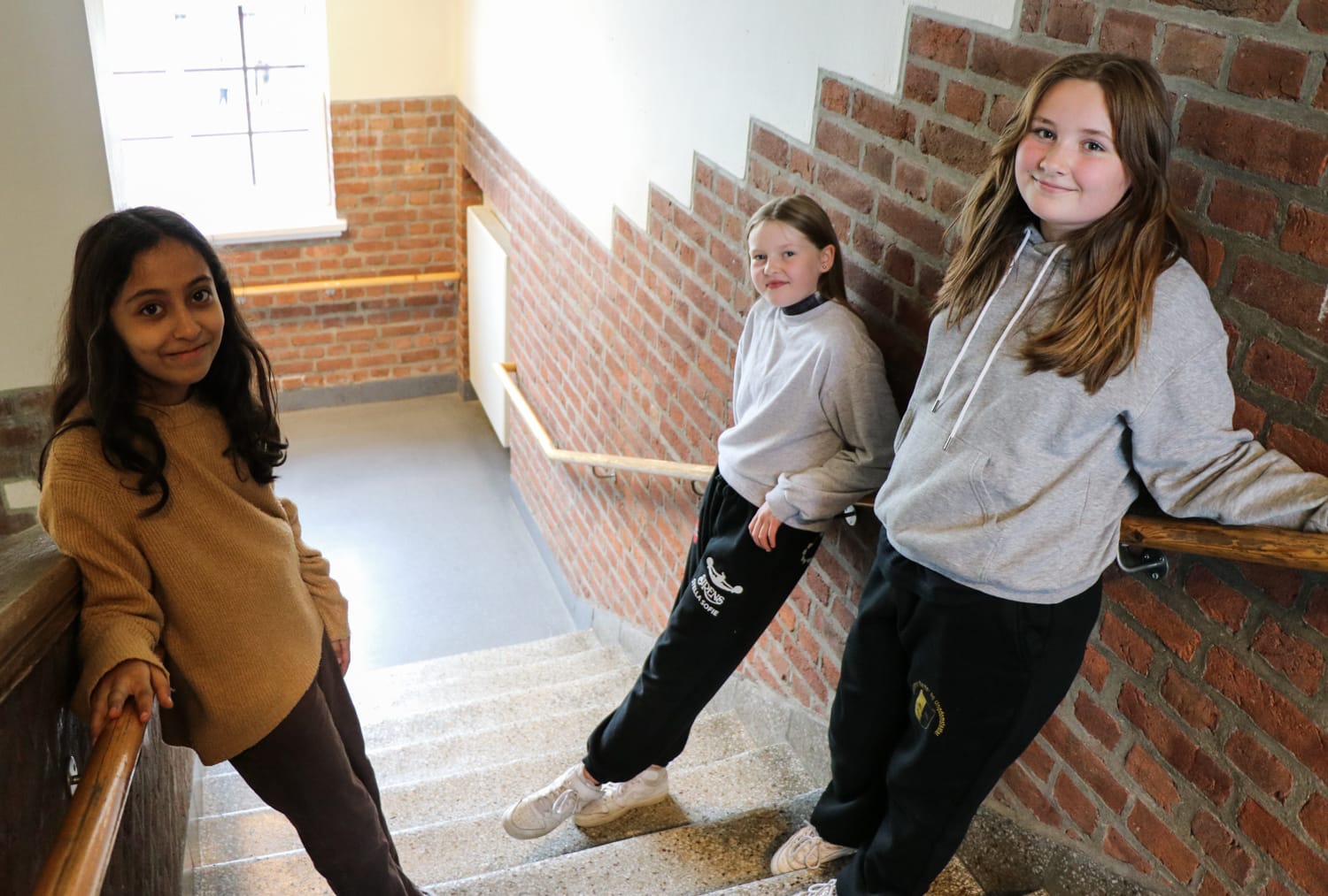 Tre jenter i 6. klasse står i trappa og lener seg mot en mursteinsvegg på Brandengen skole.