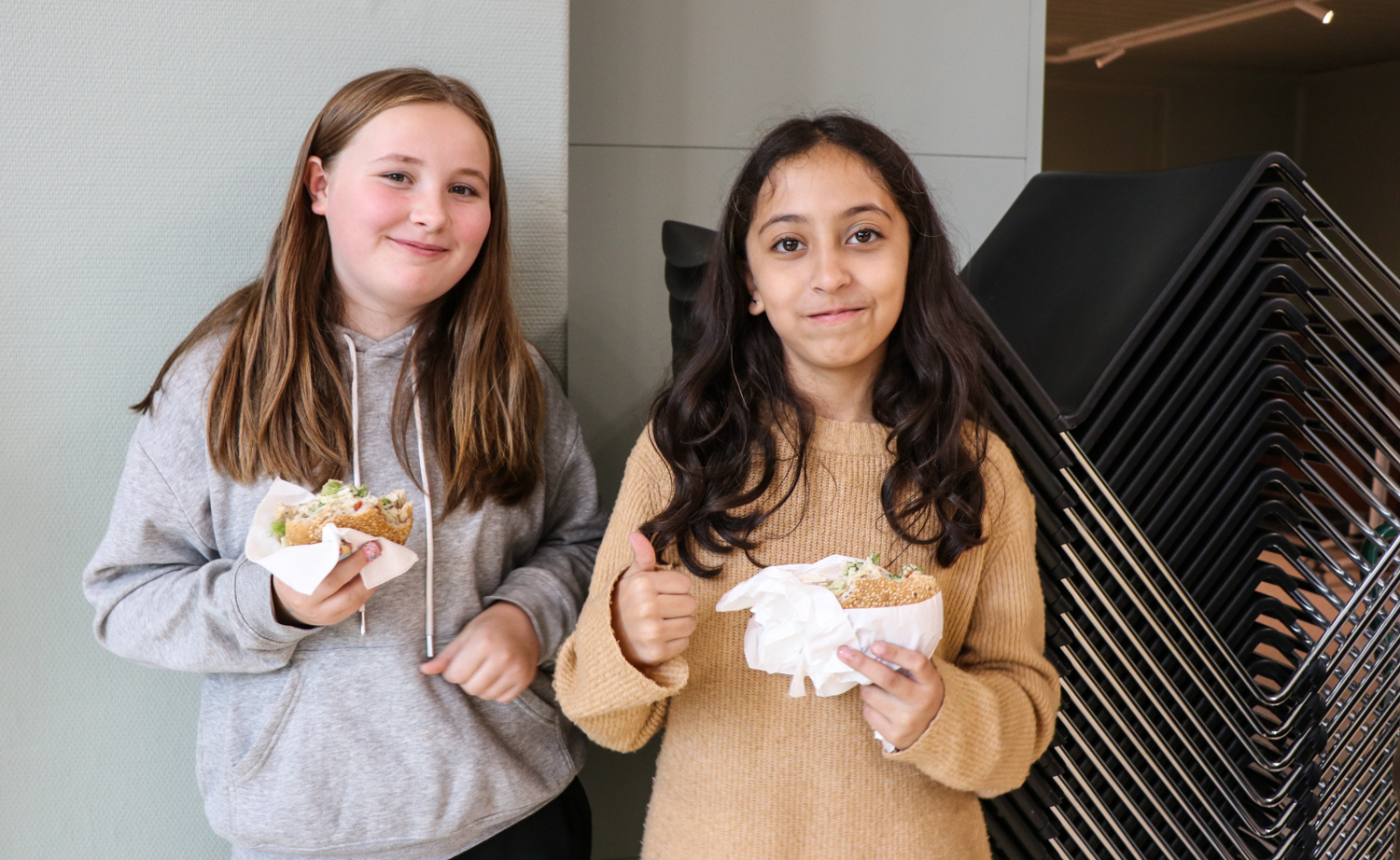 To jenter i 6. klasse smiler til kameraet og spiser fiskeburger.