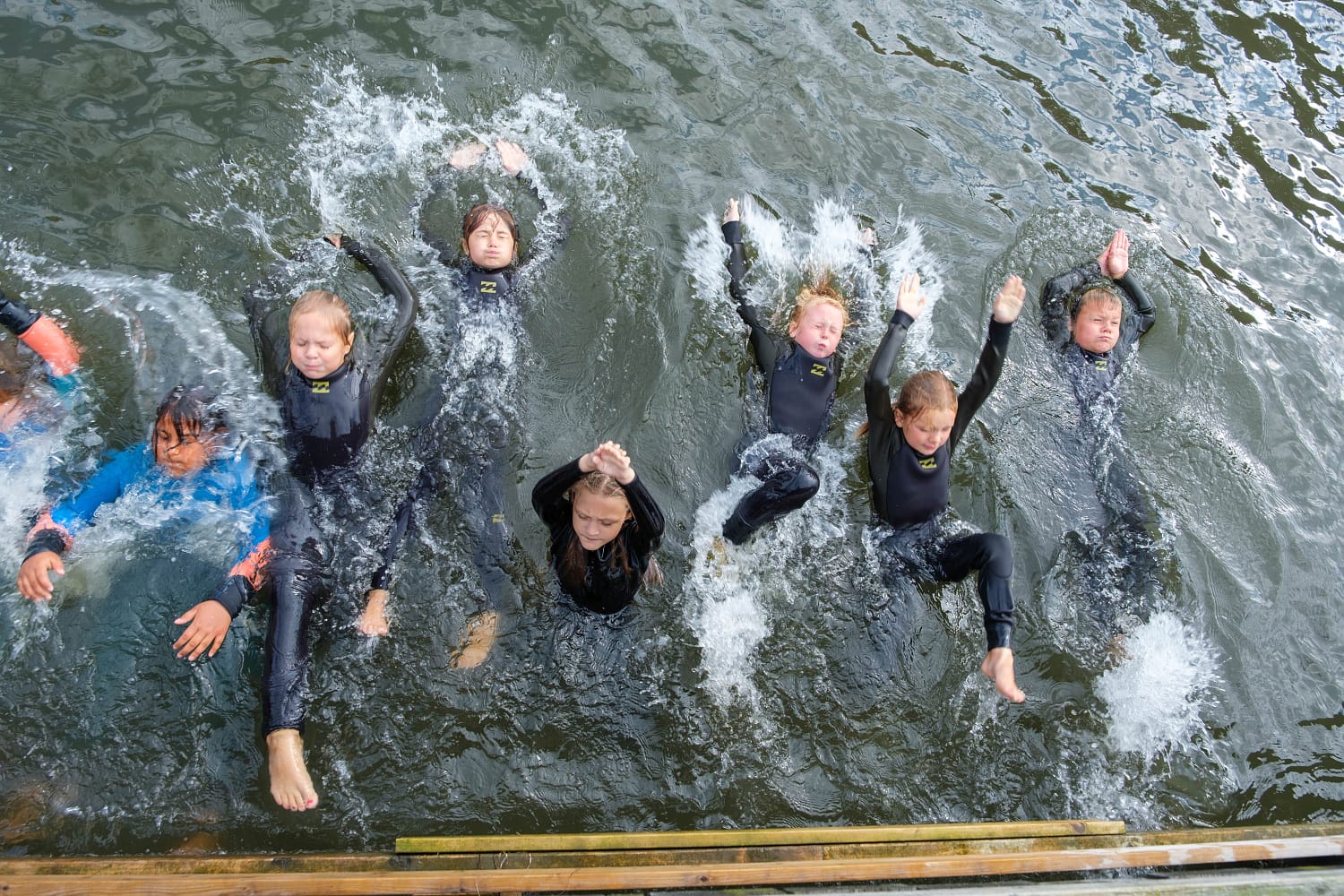 ti elever i vannet som svømmer på ryggen iført våtdrakter