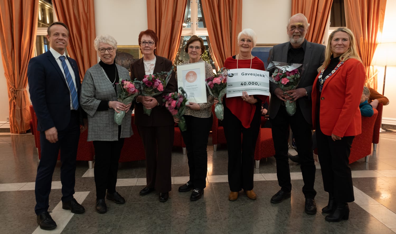 Bilde av ordfører og politiker Mads Hilden sammen med prisvinnerne i storstua på rådhuset.