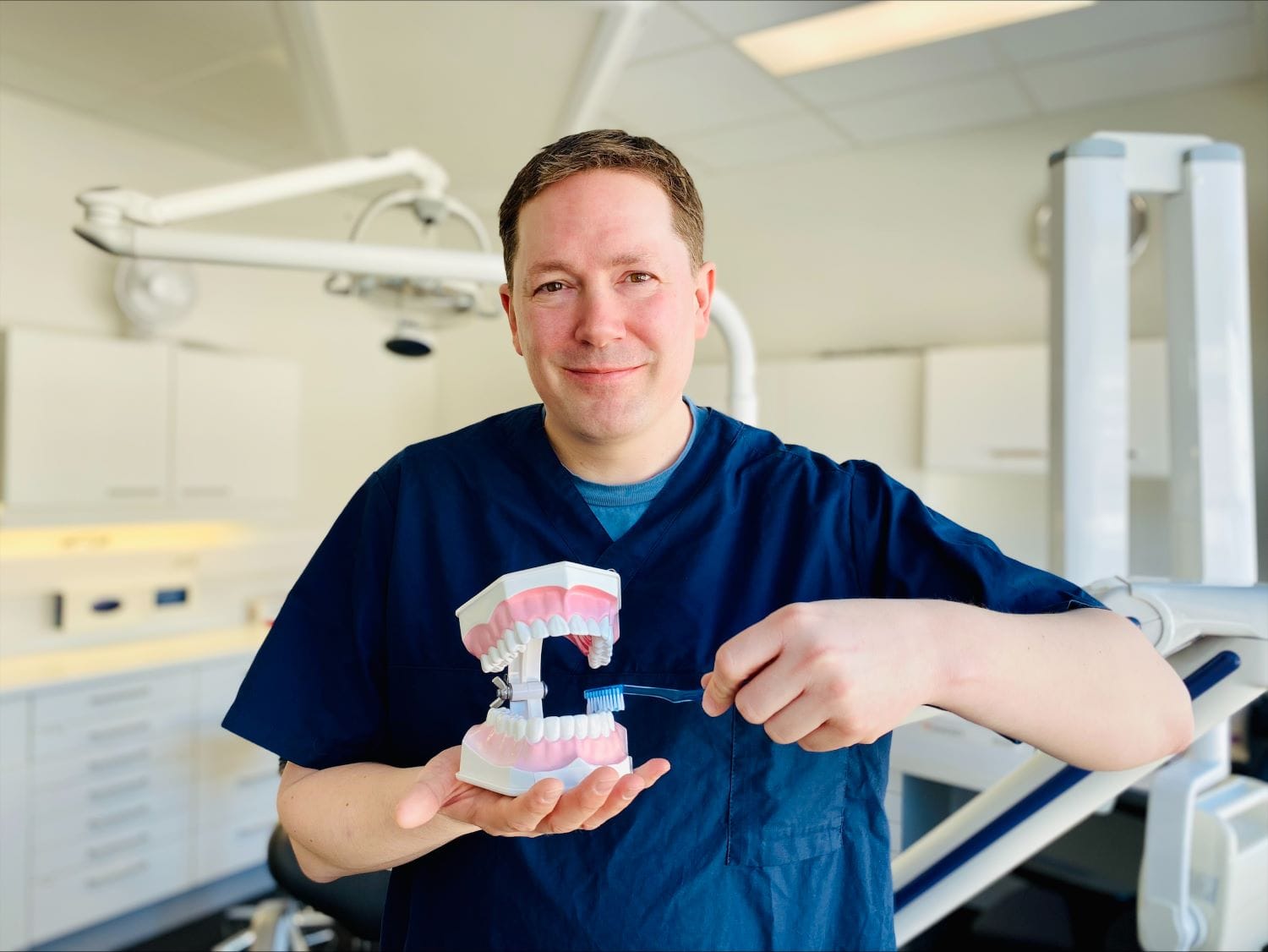 Tannpleier Leivestad står inne på et tannlegerom med en modell av tenner i hendene.