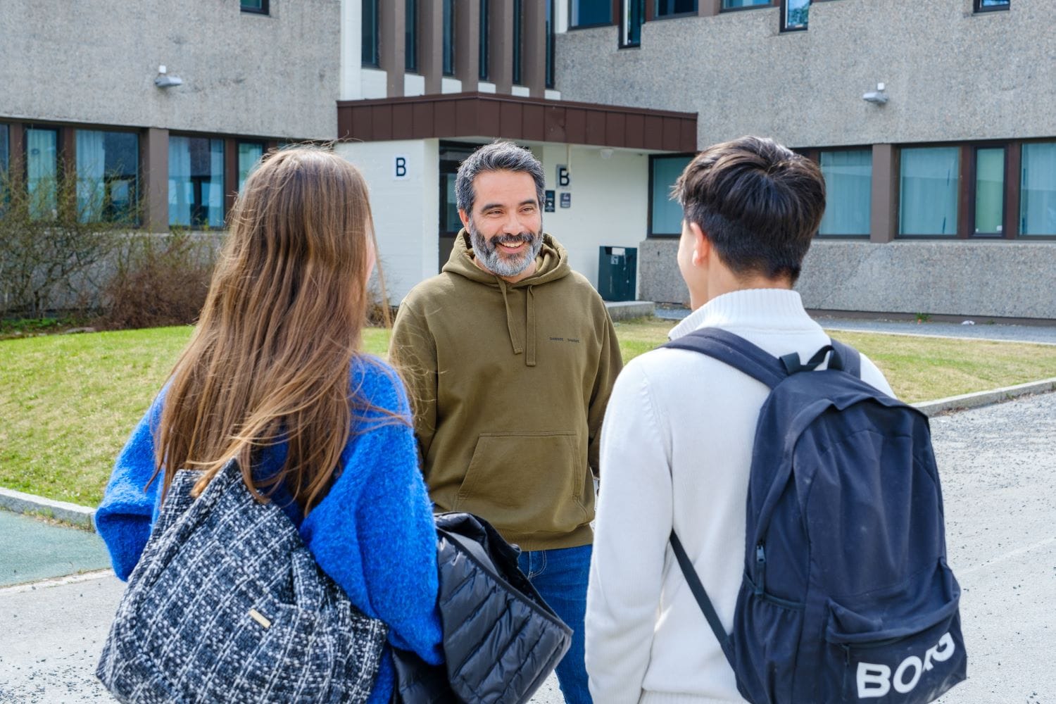 en mann prater med to ungdommer med ryggen til, som står utenfor Galterud skole