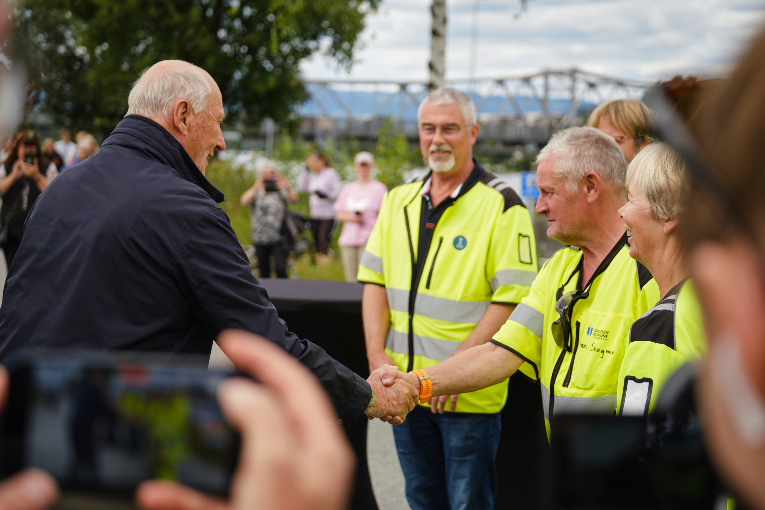 Kong Harald hilser på tre fem ansatte i Drammen kommune.