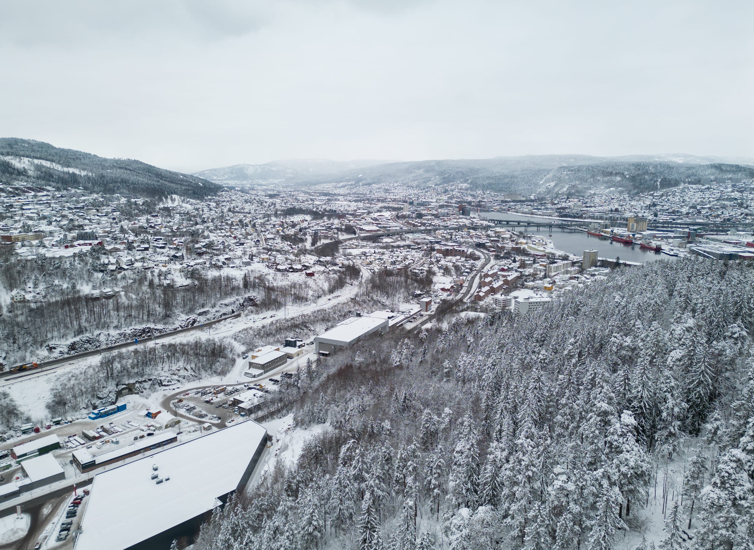 Tatt fra lufta med utsikt mot by og skog som er dekket av et tynt lag snø.