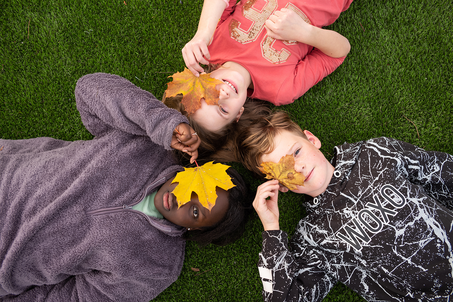 tre elever ligger med hodene mot hverandre med blader fra tær over øynene