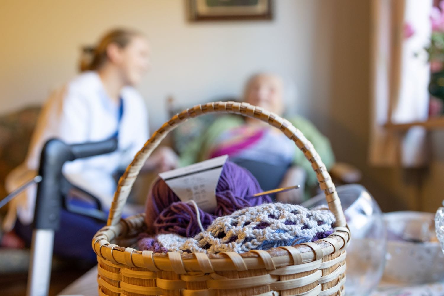 En kurv med strikketøy står i forkant av en beboer og en ansatt på sykehjem
