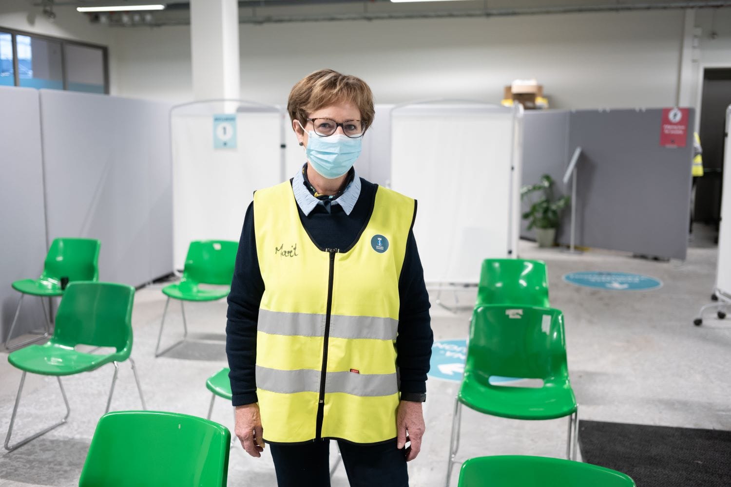 SYkeplier med vest og munnbind i vaksineringslokalen på GUlskogen. Bak henne står det grønne stoler.