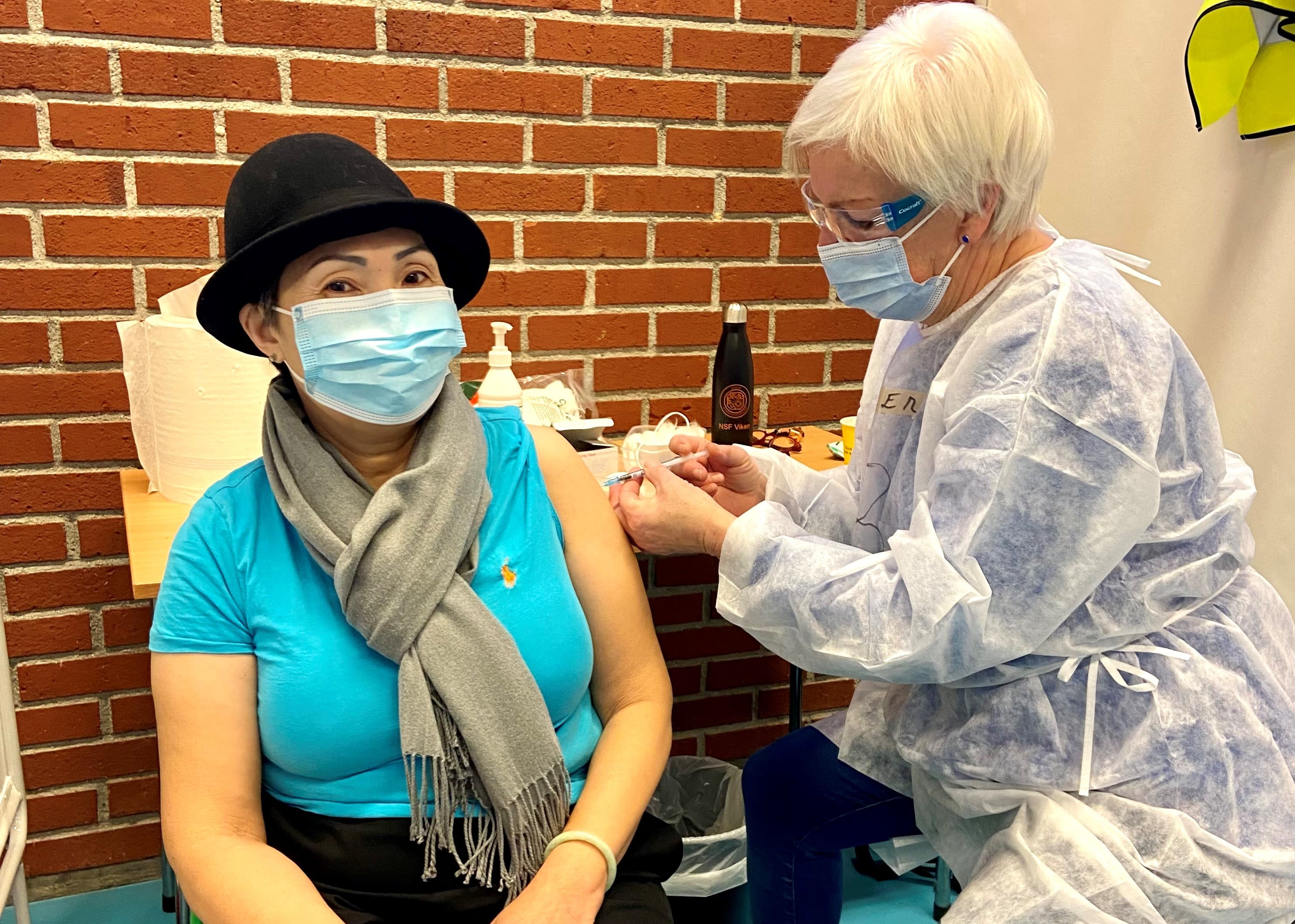 En sykepleier setter vaksine på en innbygger. Med munnbind og vernebriller
