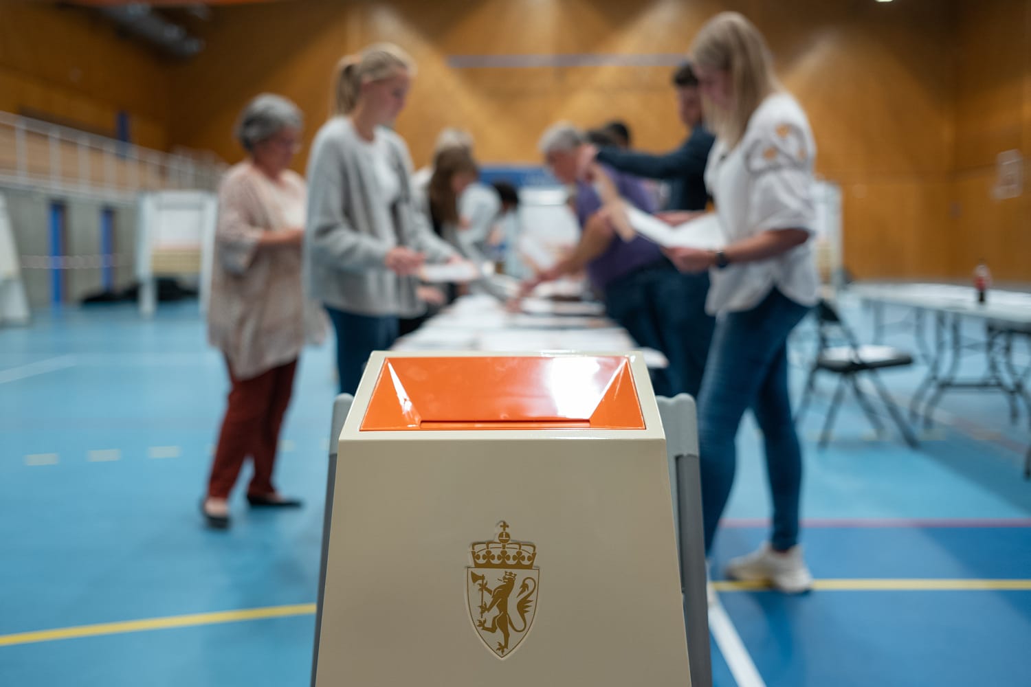 Nærbilde av valgurne med mennesker som teller stemmesedler i bakgrunnen.