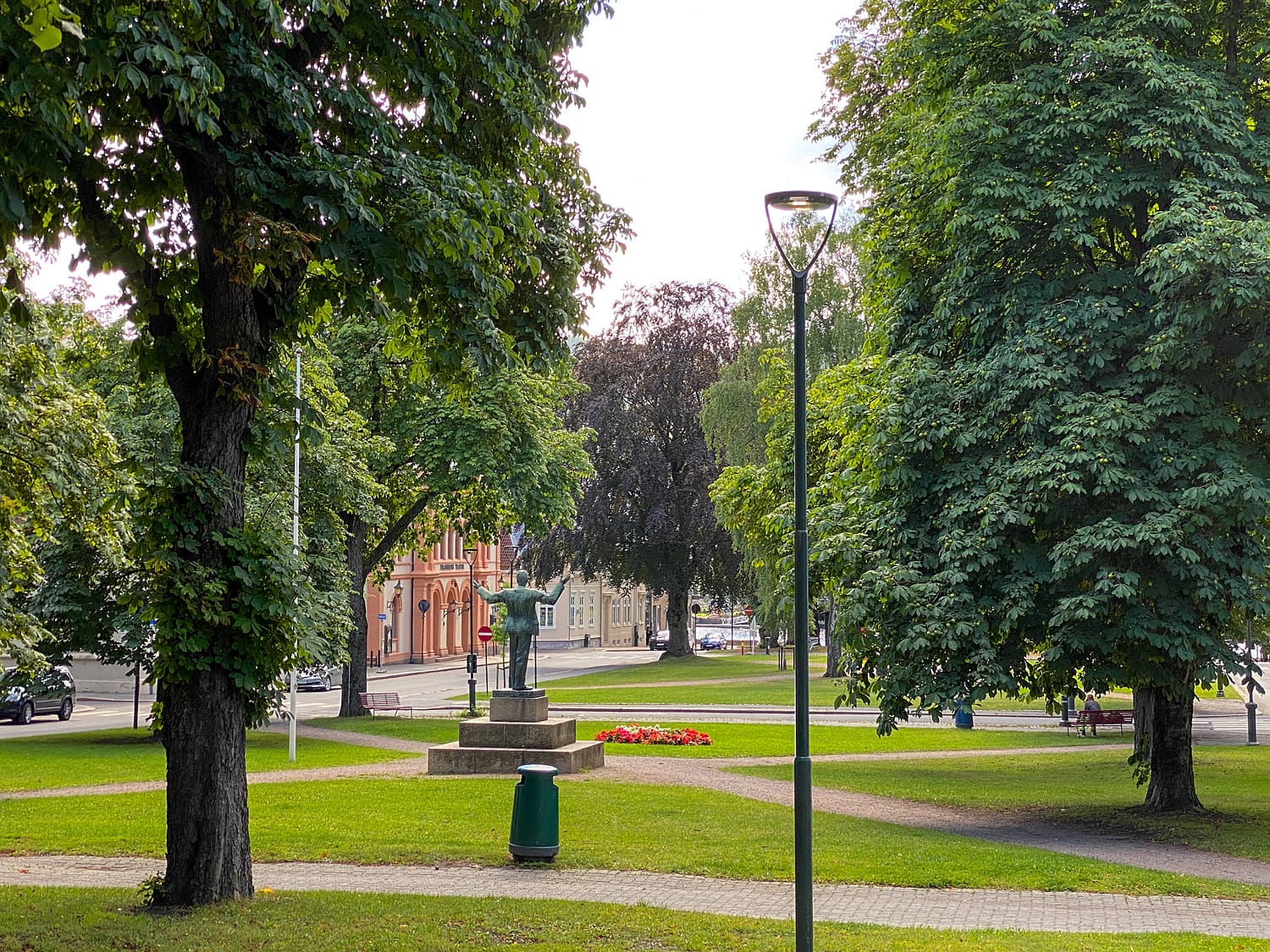 Bilde som viser Gamle Kirkeplass med park i midten og Drammen teater på venstre side. Trær i forgrunnen.