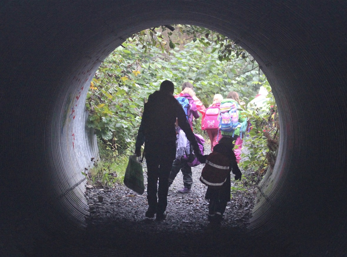 Voksen og elev hånd i hånd på tur gjennom en tunnel